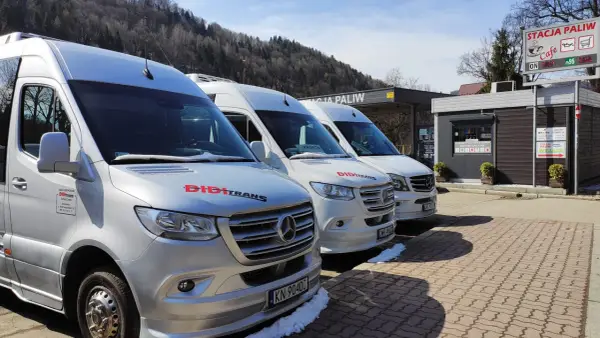 Trzy białe busy marki Mercedes stojące pod zadaszeniem stacji paliw.